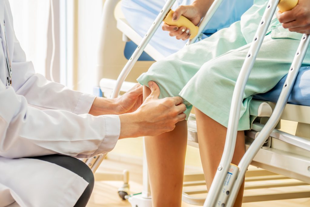 Male Doctor or Physiotherapist examining knee, female patient with injured leg or knee after catastrophic accident