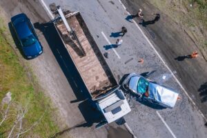 Aerial view of a serious truck accident involving a flatbed commercial truck and a heavily damaged white van, with several people standing near the crash scene.